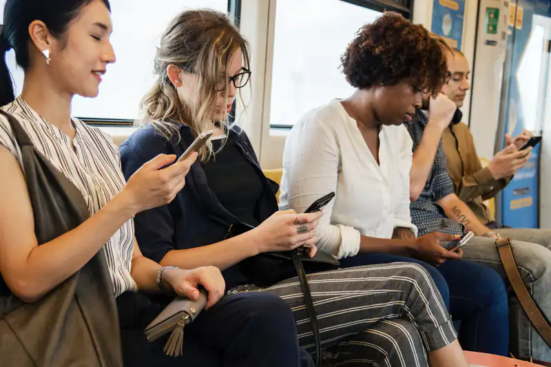 Commuters sitting in a row on a train, each checking a smartphone